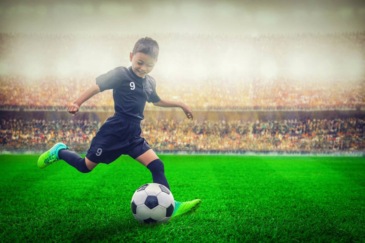 Niño pateando un balón en una cancha de fútbol