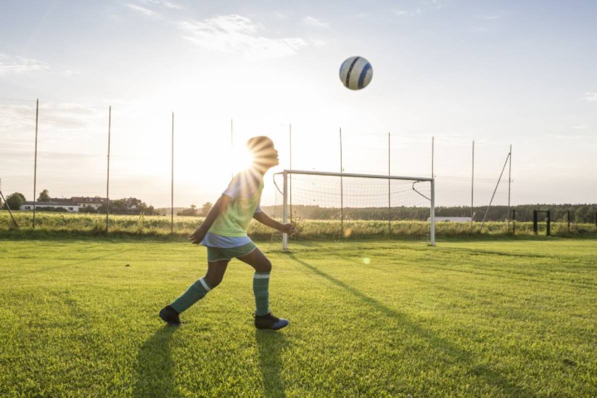 Niño jugando con la pelota y el sol está de fondo